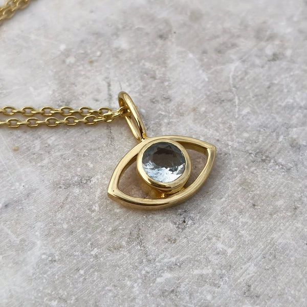An eye-shaped gold necklace with faceted aquamarine pendant on a gray surface