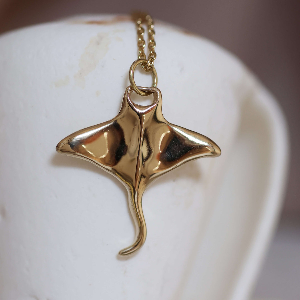 Golden brass manta pendant on a chain against a white background