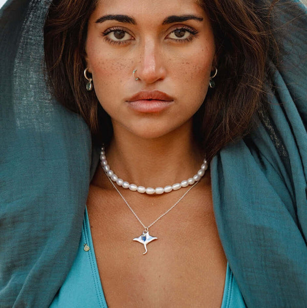 Soulshine Gems jewelry worn by a beautiful woman in turquoise aqua swimsuit - wearing manta pendant and pearl chocker necklace , and Kyanite earrings on round silver hoops.