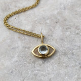 An eye-shaped gold necklace with faceted aquamarine pendant on a gray surface
