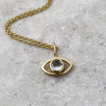 Load image into Gallery viewer, An eye-shaped gold necklace with faceted aquamarine pendant on a gray surface
