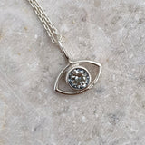 Silver necklace with a eye-shaped pendant featuring a light blue aquamarine gemstone on a marble surface