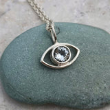 Silver eye-shaped pendant with an aquamarine gemstone on a chain, placed on a green stone.