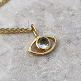 An eye-shaped gold necklace with faceted aquamarine pendant on a gray surface