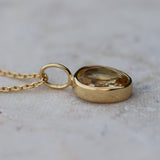 A gold citrine pendant necklace featuring a teardrop-shaped clear faceted citrine gemstone in a polished gold bezel setting, resting on a light textured surface.