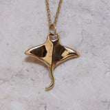 Gold manta ray pendant on a chain against a marble background