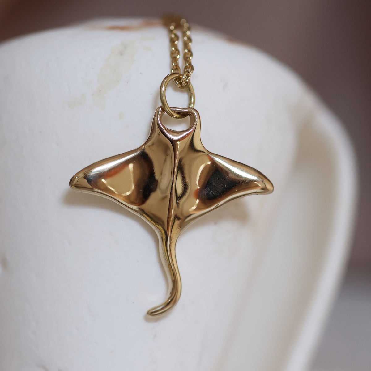 Golden brass manta pendant on a chain against a white background