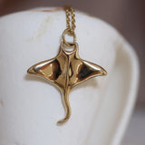 Golden brass manta pendant on a chain against a white background