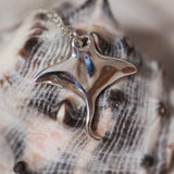 Silver manta ray pendant on a chain against a shell background