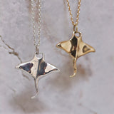 Gold and silver manta ray pendants on chains against a marble background