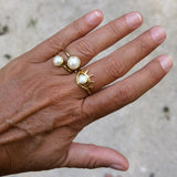 Hand wearing two gold rings with pearls and a eye shaped ring with small pearl in center on a neutral background