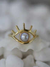 Load image into Gallery viewer, Gold ring in eye shape with a pearl in the center on a white stone background
