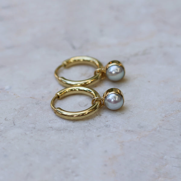 Gold hoop earrings with pearl drops on a light marble background