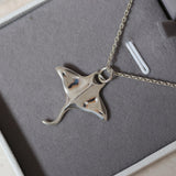 Silver manta ray pendant on a chain in a gray / white necklace box.
